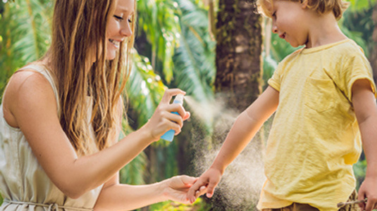 Mom spraying kids arm with sunscreen